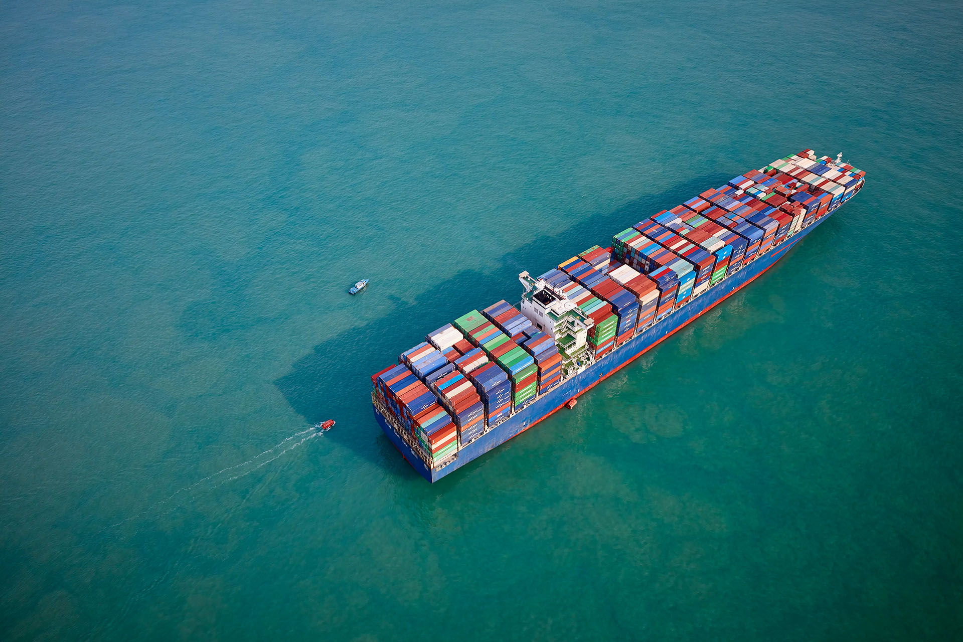 A large colourful containership at anchor in a deep turquoise sea 